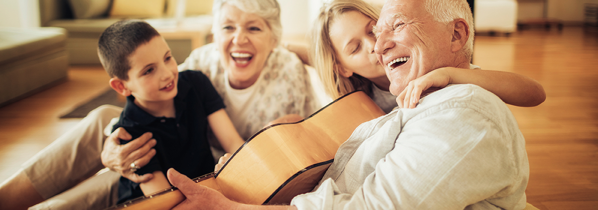 Grandparents palying guitar and laughing with younger grand son and older grand daughter.