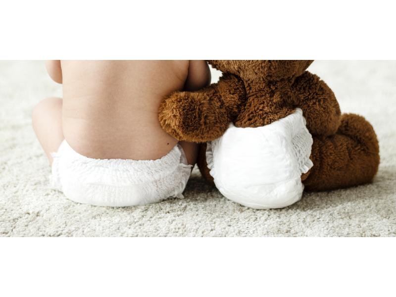 Baby in diaper sitting on a rough with a teddy bear on their side, also wearing a diaper.