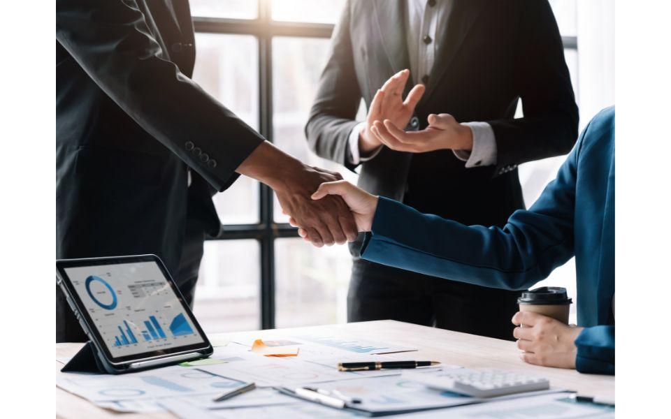 Due people shaking hands at a desk in front of a third person